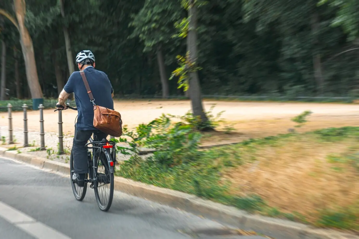 Mann fährt Fahrrad mit Tasche auf einer Stadtstraße – aktive urbane Mobilität.